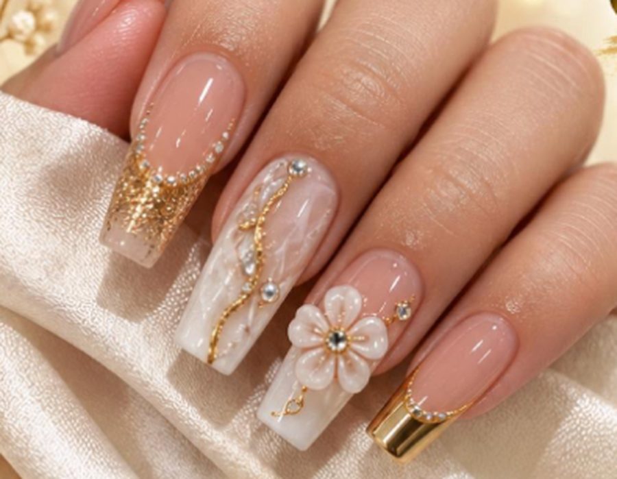 Long nude nail extensions with gold flakes, pearl details and a white flower design